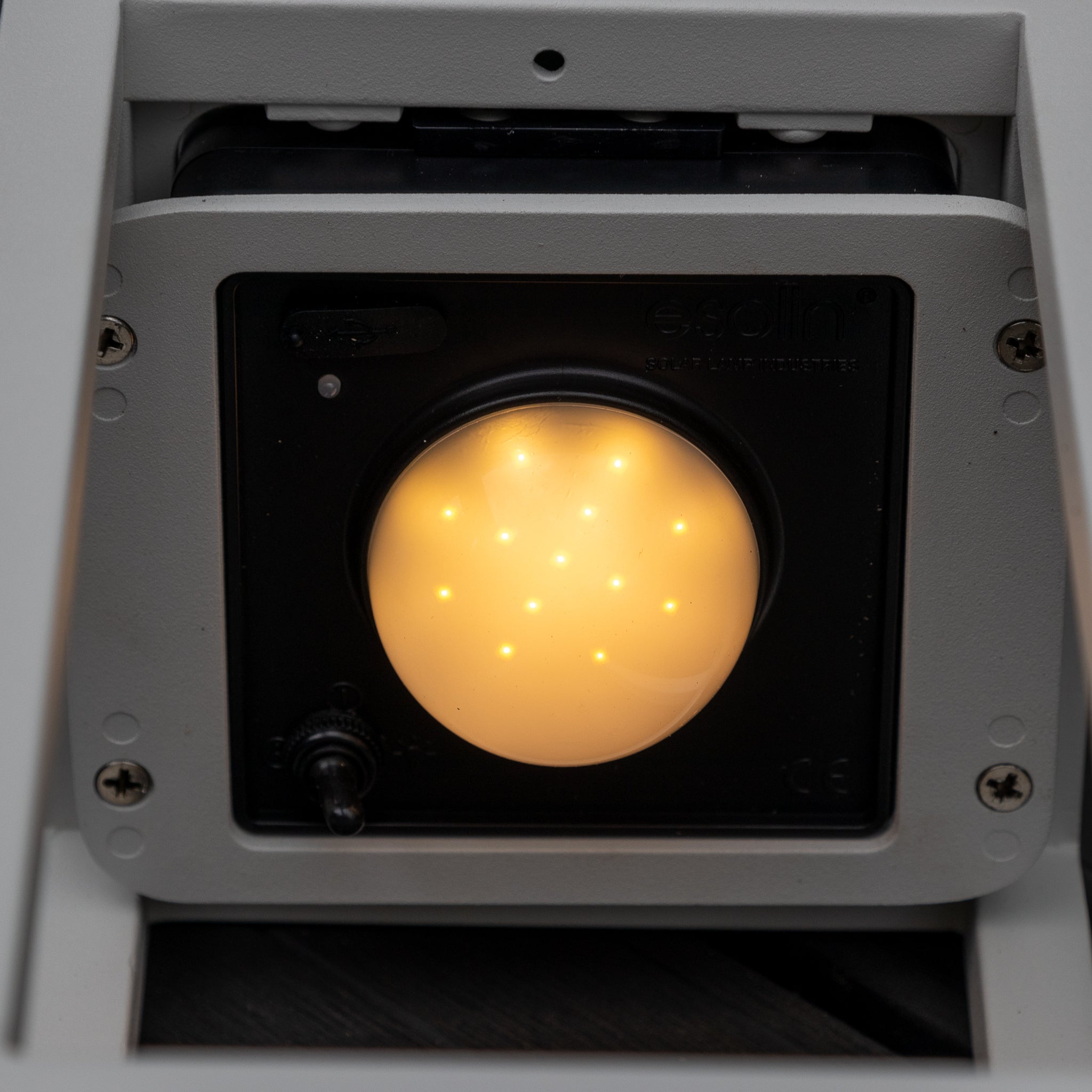 Close-up of a yellow illuminated LED indicator in the grey metallic housing with surrounding screws, perfect for the Luxor Large Floor Outdoor and Indoor Solar Lantern in Charcoal.
