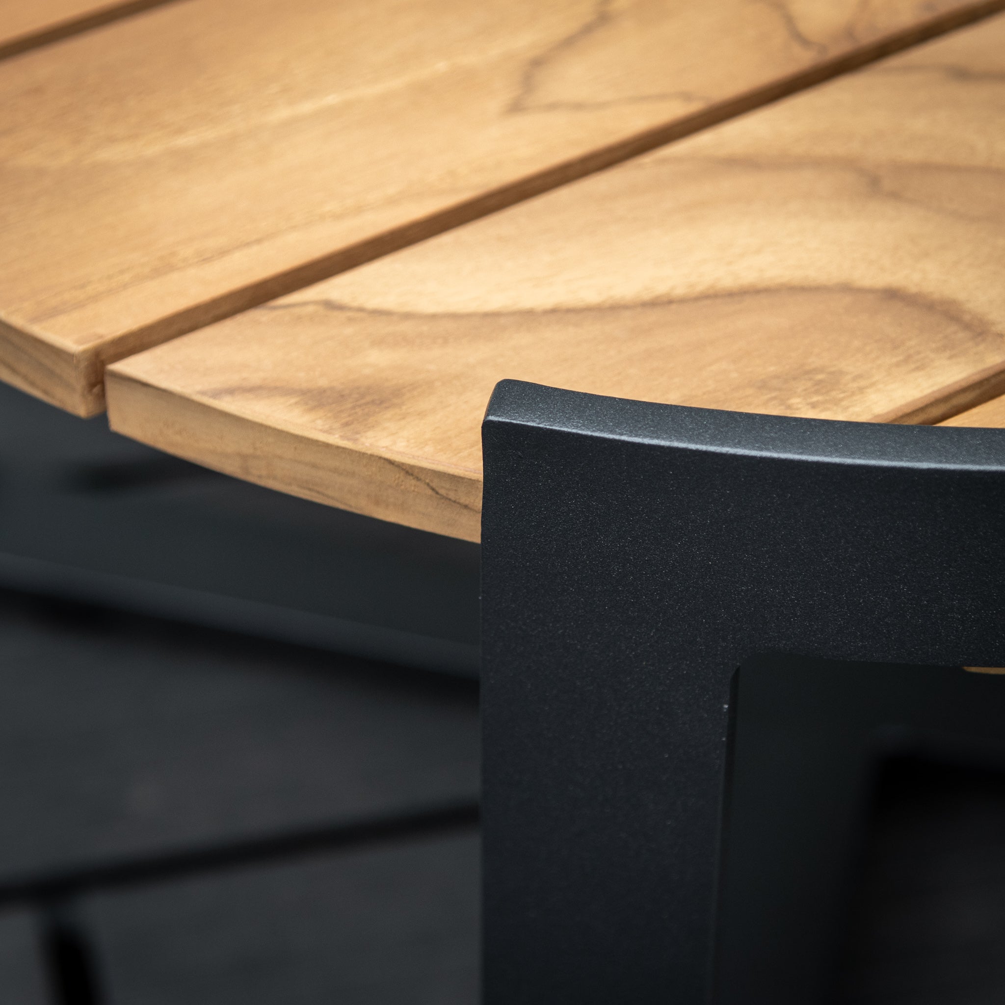 Close-up of the Bloom Coffee Table with Teak Top in Charcoal, showcasing its rich grain details and sturdy black metal legs, making it a striking piece of outdoor furniture.
