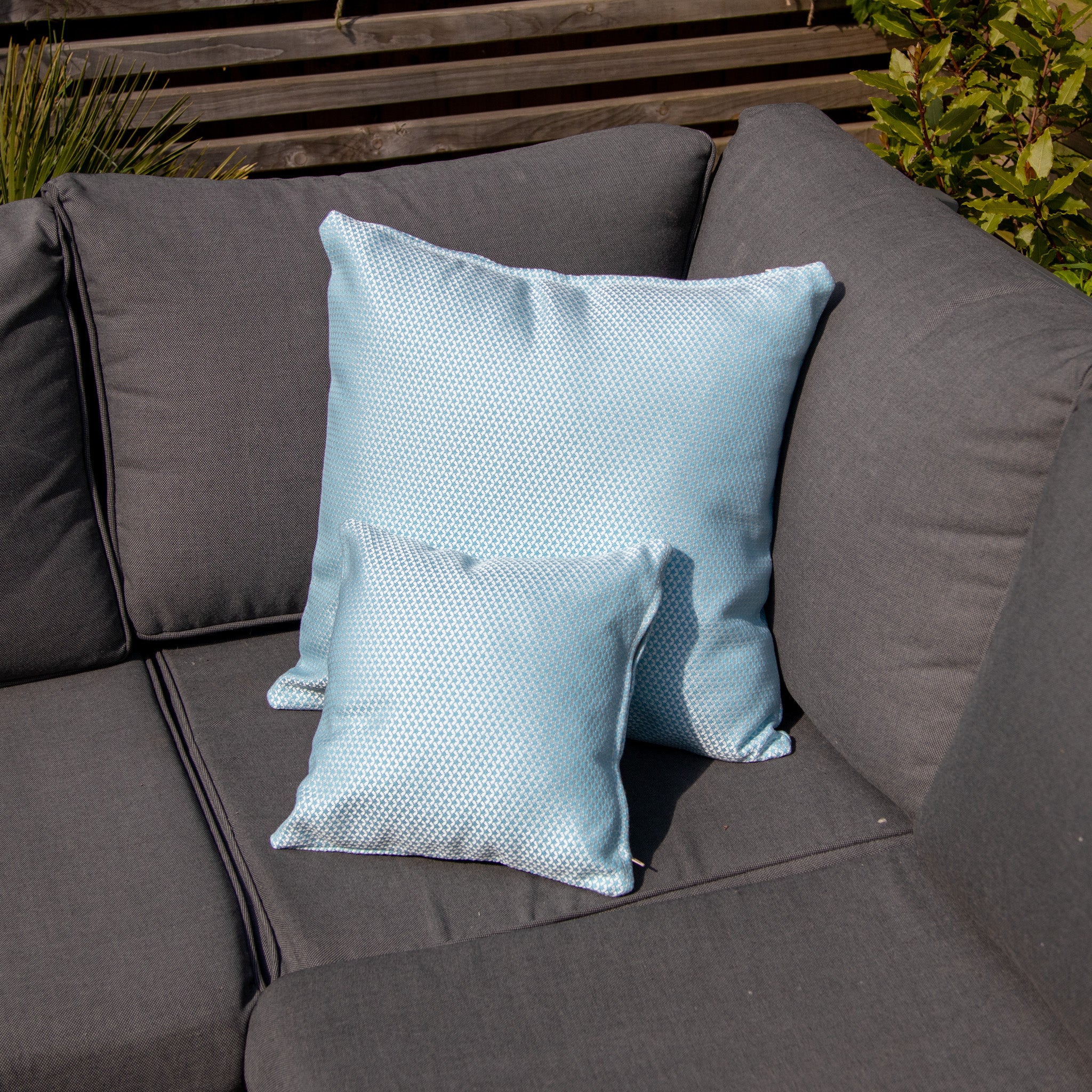 Two Agora Scala Celeste Small Scatter Cushions (25cm x 25cm) with a light blue pattern on a dark grey outdoor sofa in a shaded garden area.