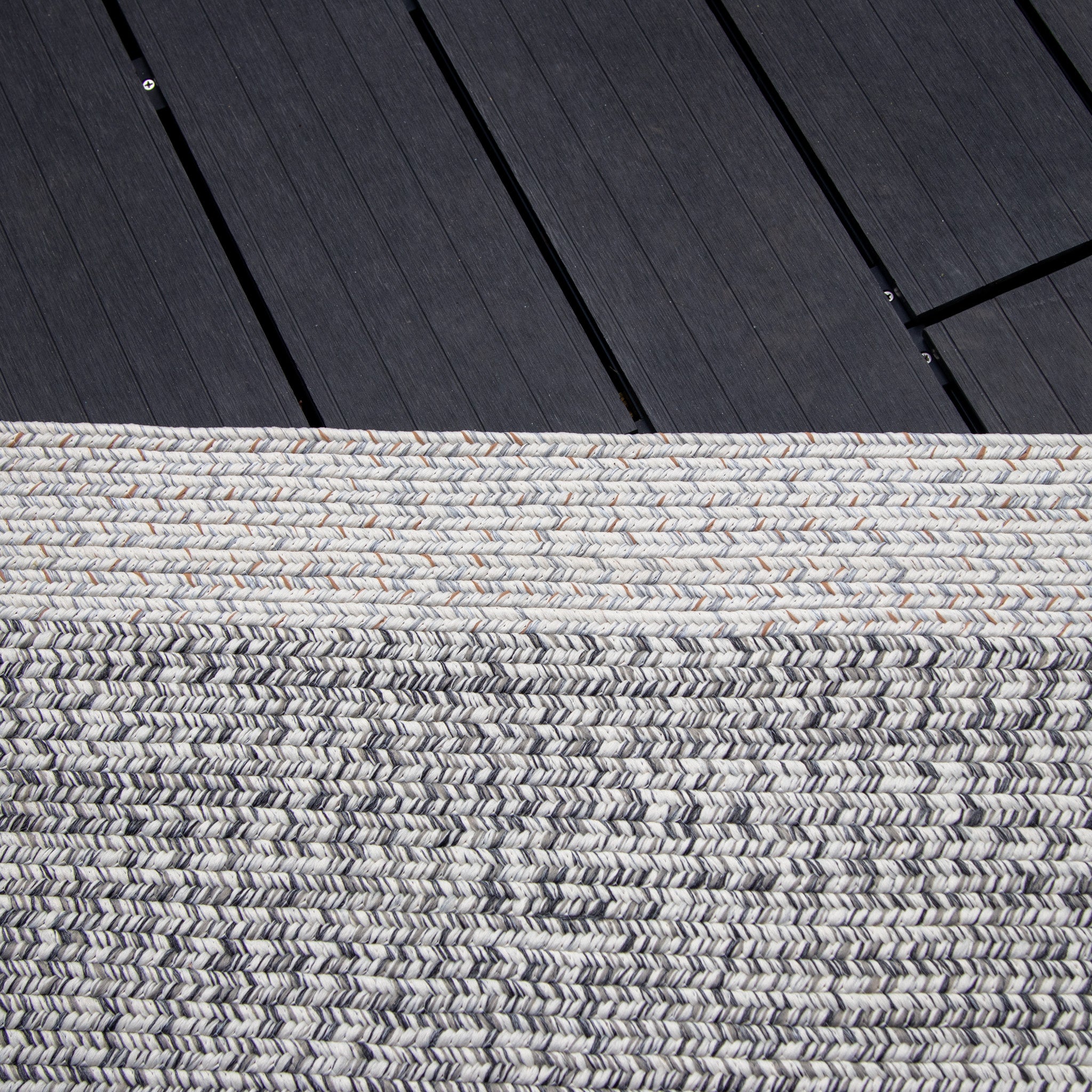 Close-up of the textured Hades 290cm x 190cm Weatherproof Indoor and Outdoor Rug in Cobble Grey on a dark wooden floor, showcasing a striking contrast between light and dark materials while highlighting its UV resistant qualities.