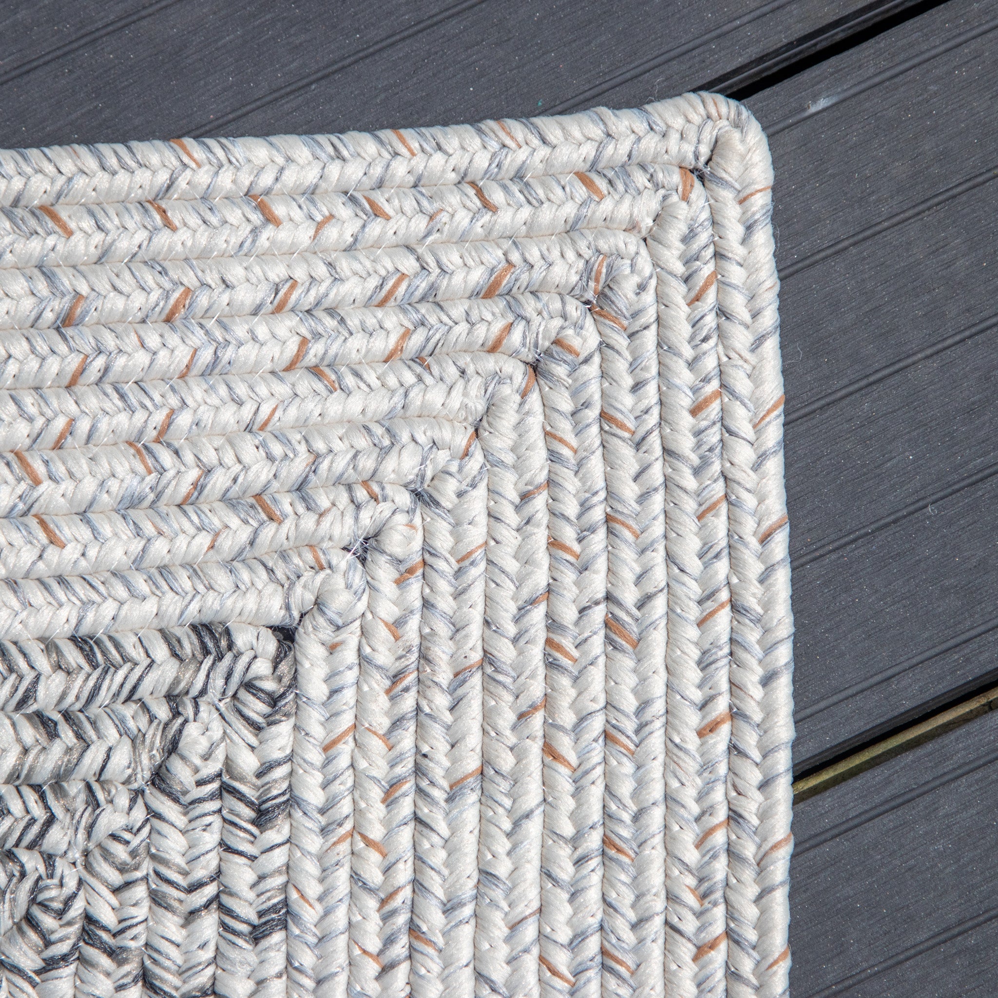 Close-up of the Hades 290cm x 190cm Weatherproof Indoor and Outdoor Rug in Cobble Grey, a woven, multicolored piece with a rectangular pattern on a gray wooden floor. This UV-resistant rug adds both durability and style to any space.
