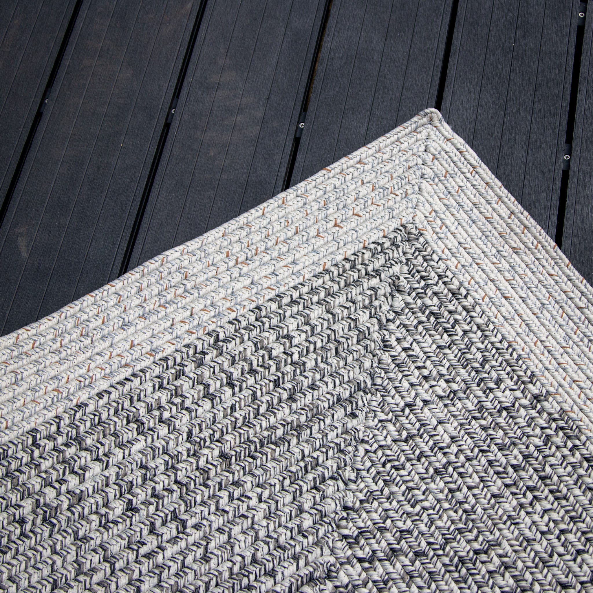 Close-up of the Hades 290cm x 190cm Weatherproof Indoor and Outdoor Rug in Cobble Grey, showcasing its textured, woven fabric with black and white patterns on a dark wooden floor.