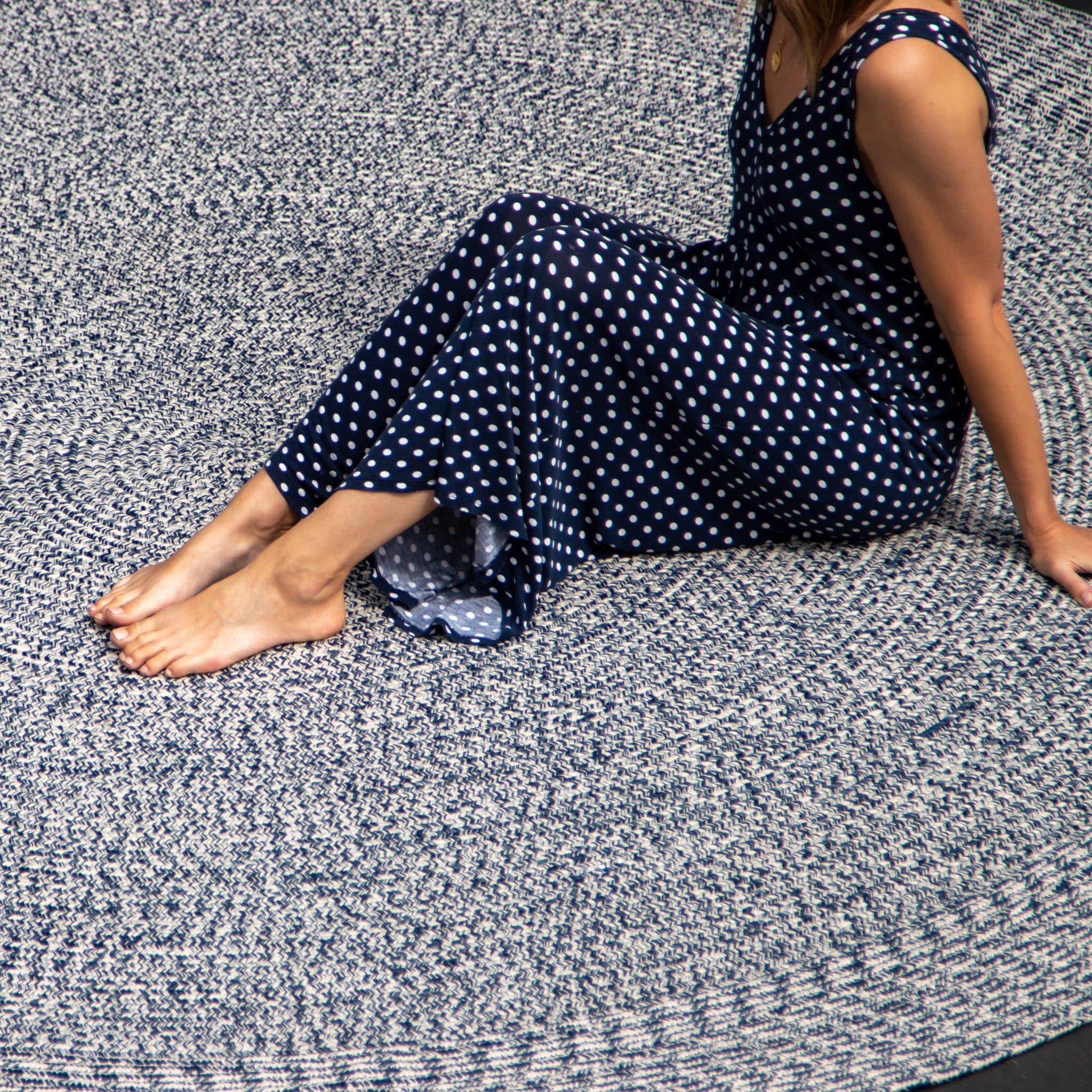 A person in a blue polka dot dress sits on the Apollo 300cm Round Indoor and Outdoor Rug in Prussian Blue with their legs stretched out, appreciating its stylish design and UV-resistant durability.