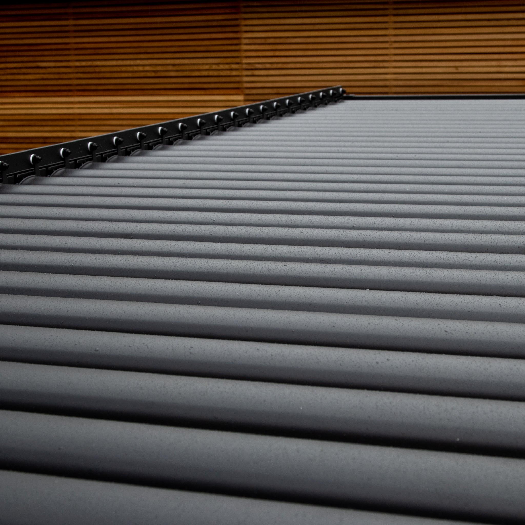 Close-up of the PergoSTET Plus 3m x 3m Square Pergola's louvred roof in grey, featuring a sleek design with LED lighting, set against a wooden wall.
