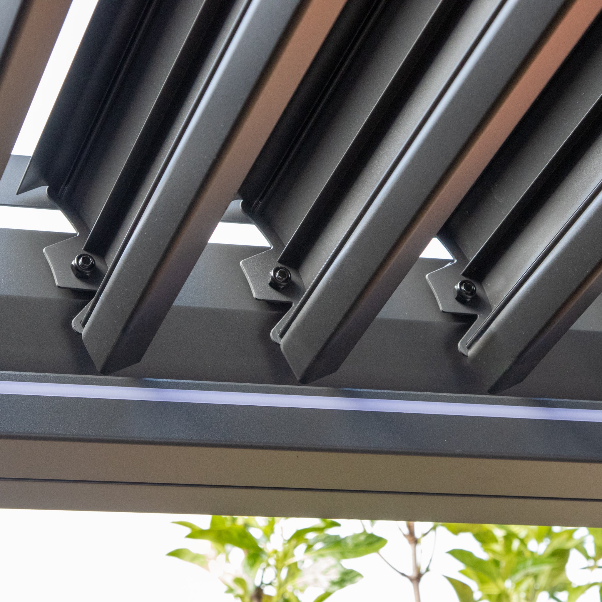 Close-up of a PergoSTET Plus with a louvered roof and metal slats partially open, featuring LED lighting that illuminates the greenery in the background.