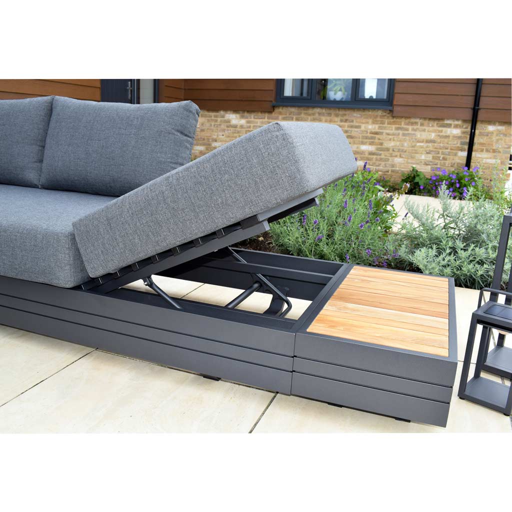 Outdoor modular sectional sofa with adjustable backrest and gray cushions on a contemporary aluminum frame, paired with a sleek Panama Teak Side Table, set on a patio with plants in the background.