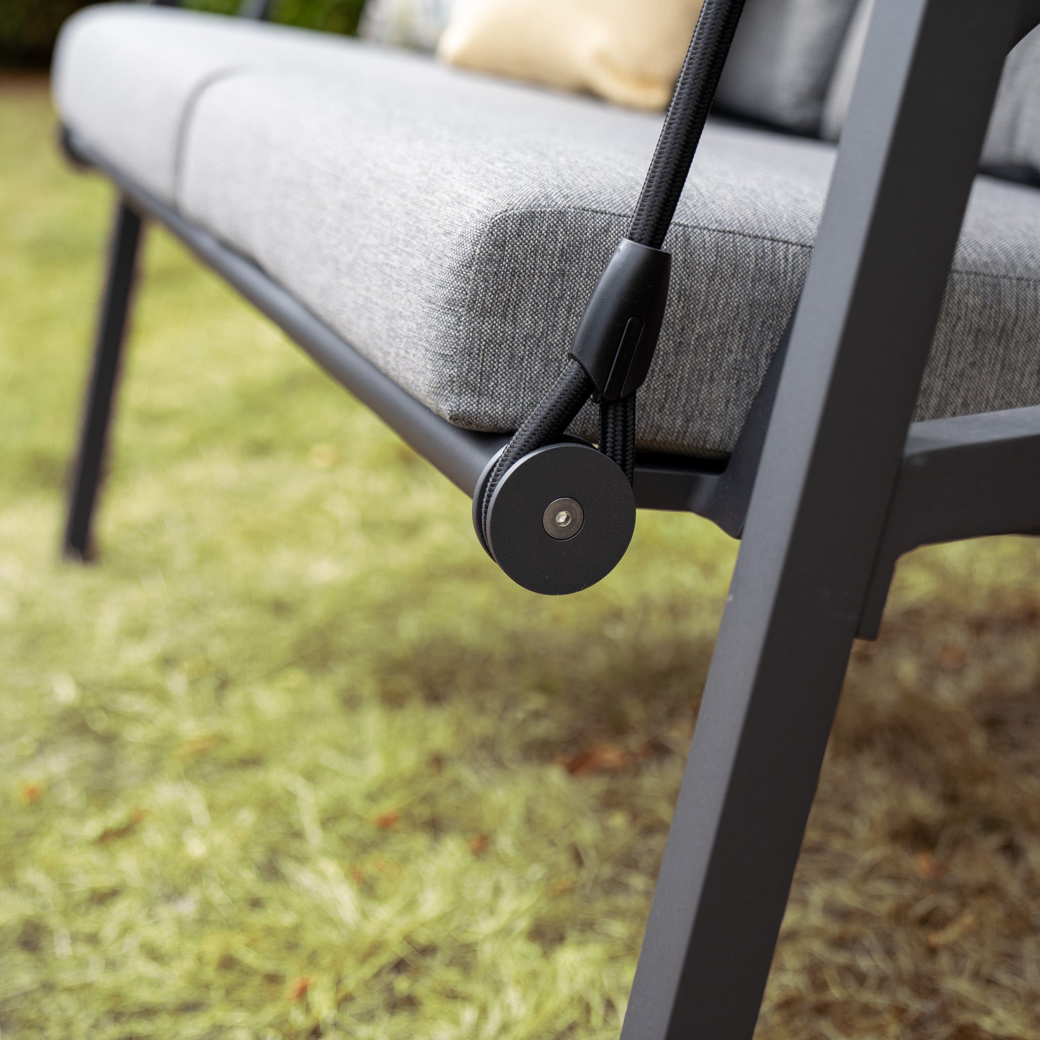 Close-up of the Lima Aluminium Swing Seat in Washed Grey, showcasing a small pulley mechanism on the side and a powder-coated aluminium frame, set over grass.