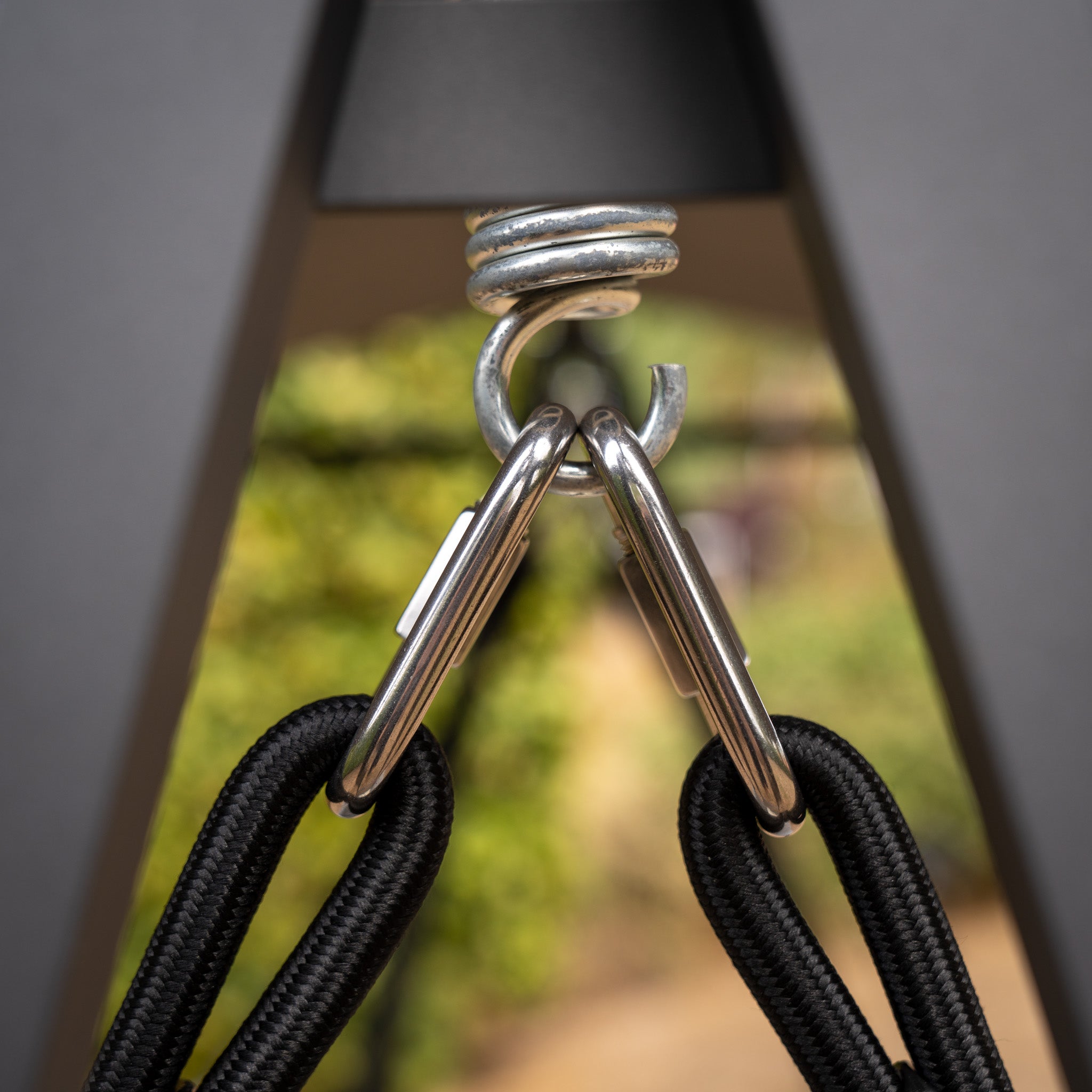 Close-up of the Lima Aluminium Swing Seat in Washed Grey, featuring carabiners attached to an overhead ring with black ropes, set against a blurred outdoor background. This showcases the durable construction and sleek design typical of powder-coated aluminium frames.