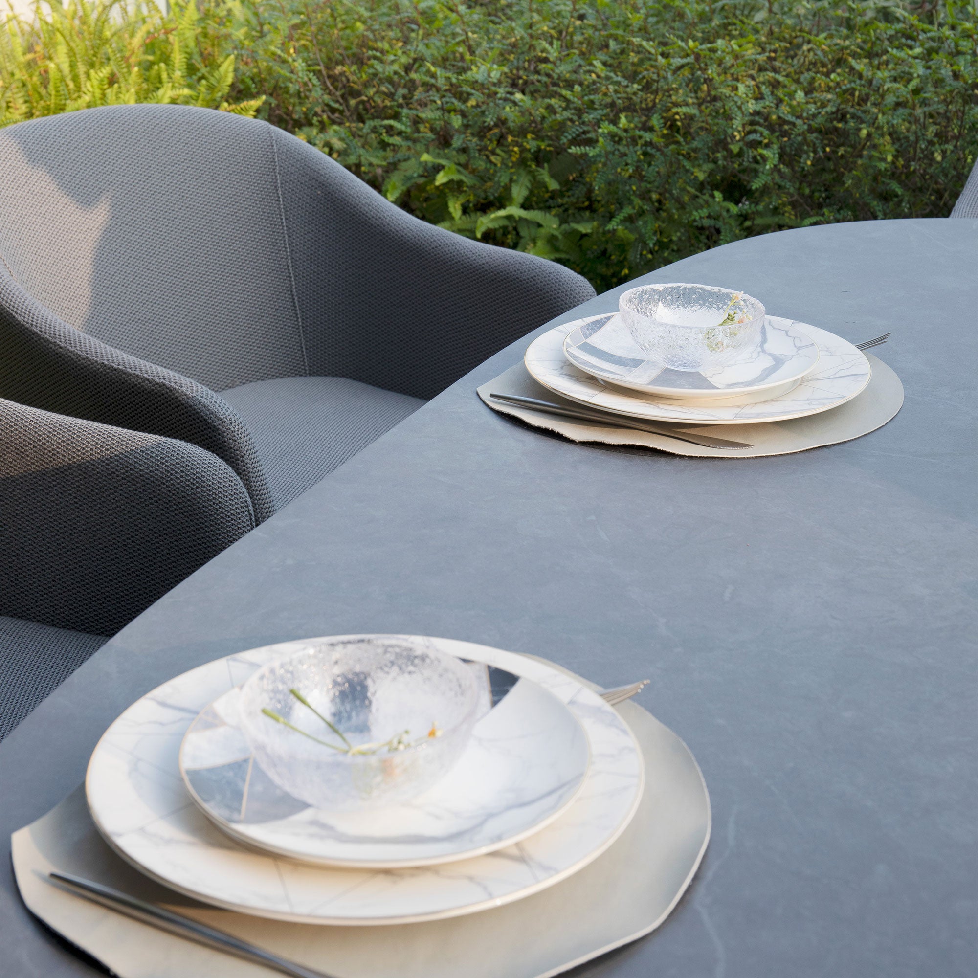 Introducing the Luna 6 Seat Outdoor Fabric Oval Ceramic Dining Set in Grey, featuring two place settings with elegant white dishware and grey chairs crafted from all-weather material.