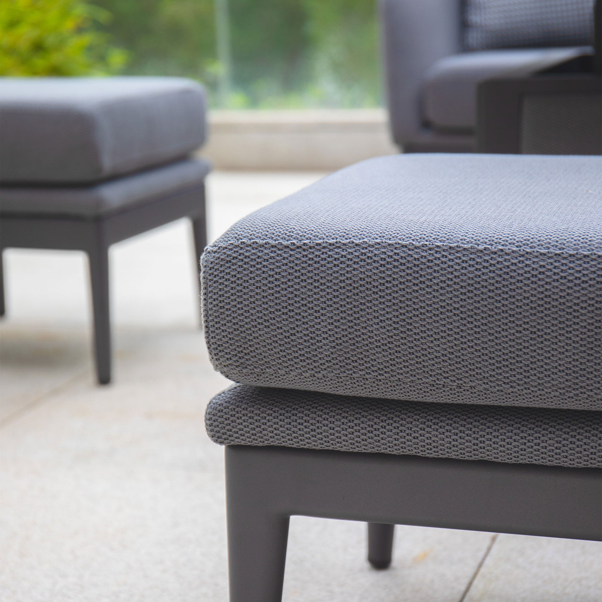 Close-up of modern outdoor gray cushioned seating on a patio with a blurred green background, featuring the elegant Luna Outdoor Fabric Rectangular Corner Dining Set with Rising Table in Grey (Right Hand) by Harbour Lifestyle.
