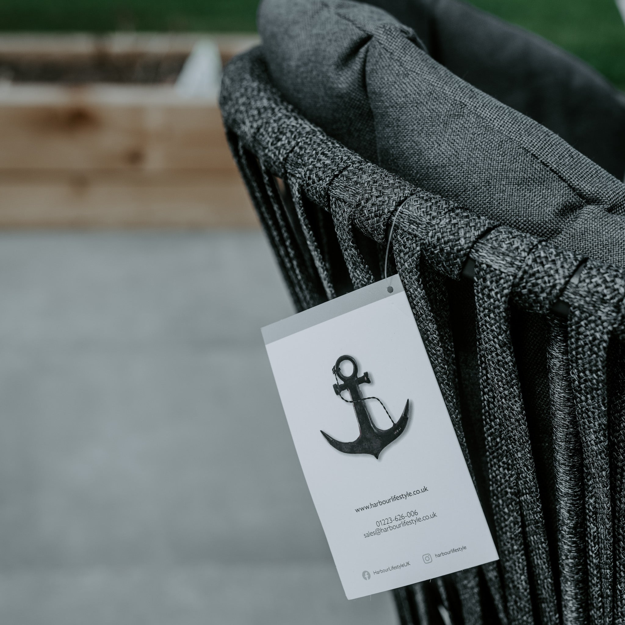 Here is a close-up of a gray woven chair, a component of the Monterrey 8 Seat Rope Dining Set with Oval Ceramic Table in Grey from Harbour Lifestyle. The tag displays an anchor logo along with contact information. This piece integrates seamlessly with outdoor rope dining chairs and the ceramic glass dining table from the same set.
