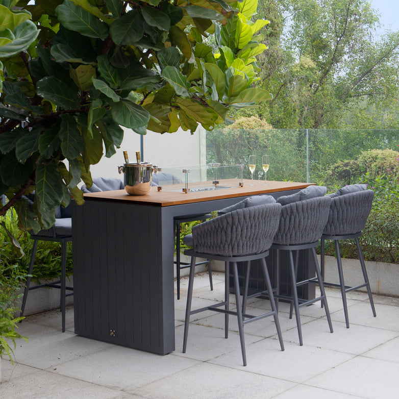 The outdoor patio features a Palma 6 Seat Rope Teak Firepit Bar Set in Grey from Harbour Lifestyle, complete with wine and an ice bucket, surrounded by lush greenery. This addition enhances the entire experience.
