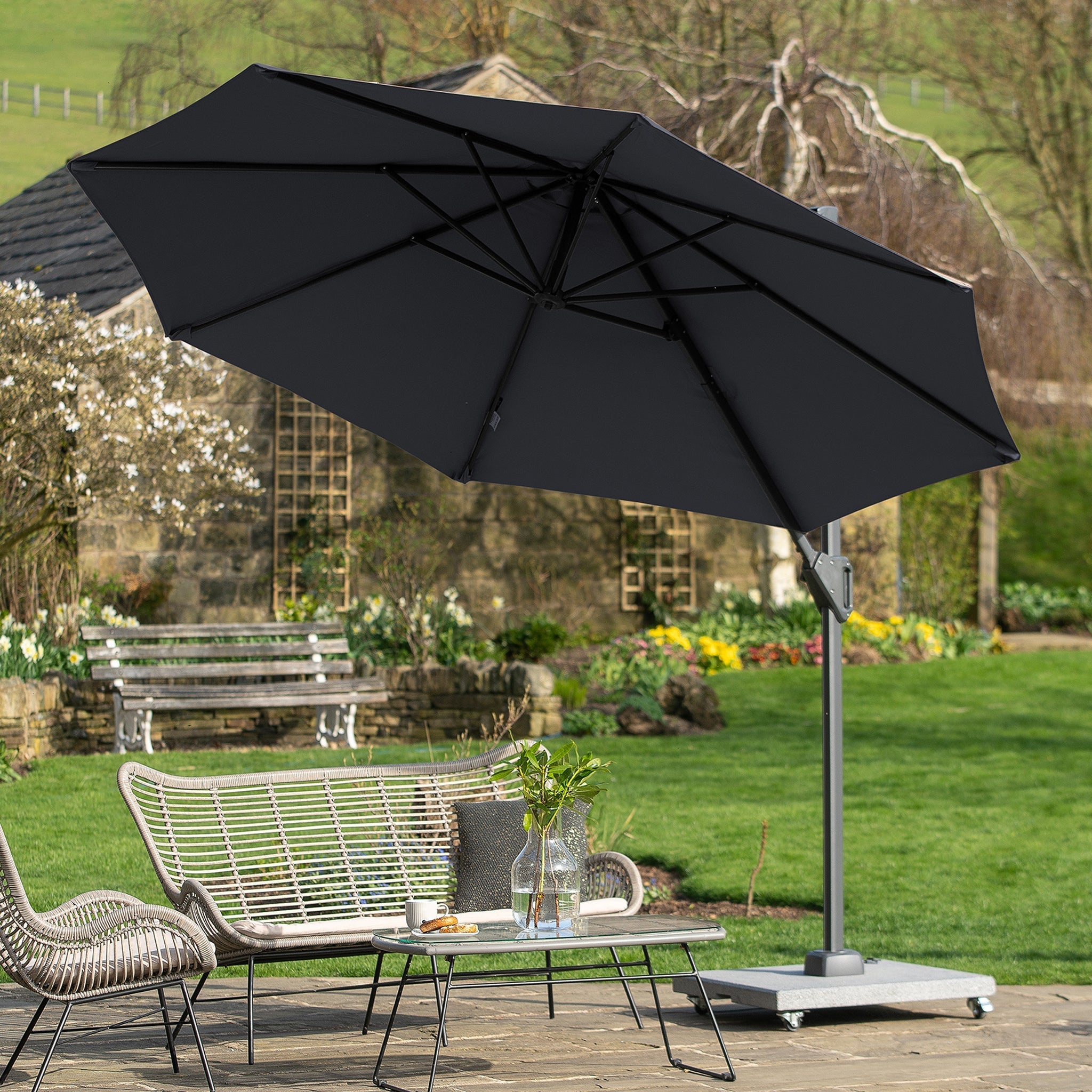 The patio includes a Pacific Lifestyle Voyager T1 3m Round Parasol in Anthracite, shading the wicker furniture and decorative plants in a charming garden setting.