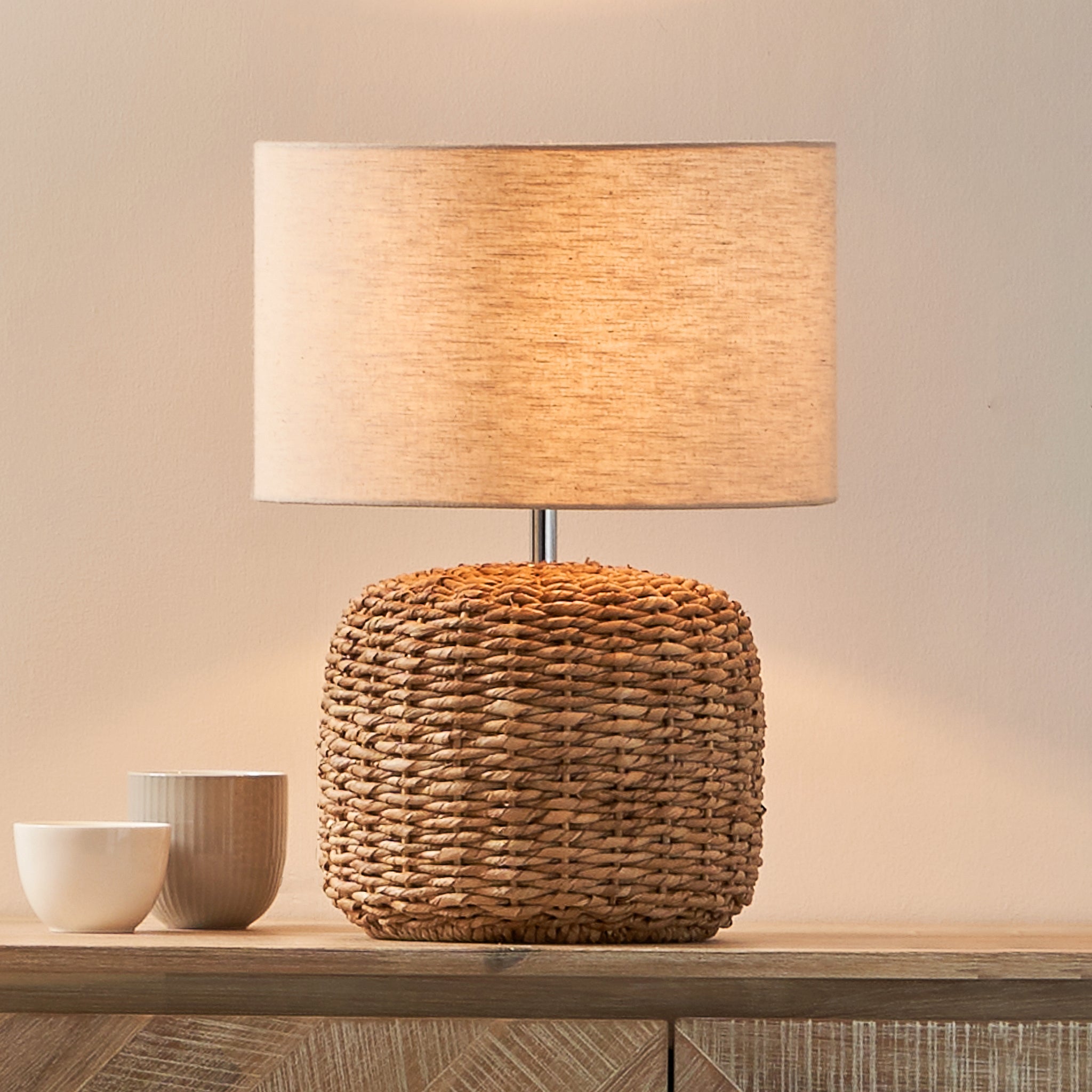 The Pacific Lifestyle - Acer Natural Woven Small Table Lamp in Ivory sits on a wooden surface beside two ceramic bowls, creating a rustic look.