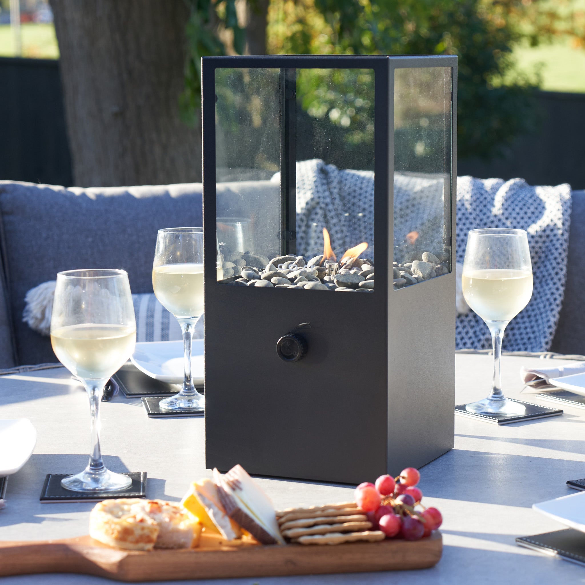 The Cosi - Cosidome High Black Fire Lantern graces the table alongside wine glasses and a cheese board, exuding a minimalistic design that's ideal for outdoor gatherings.