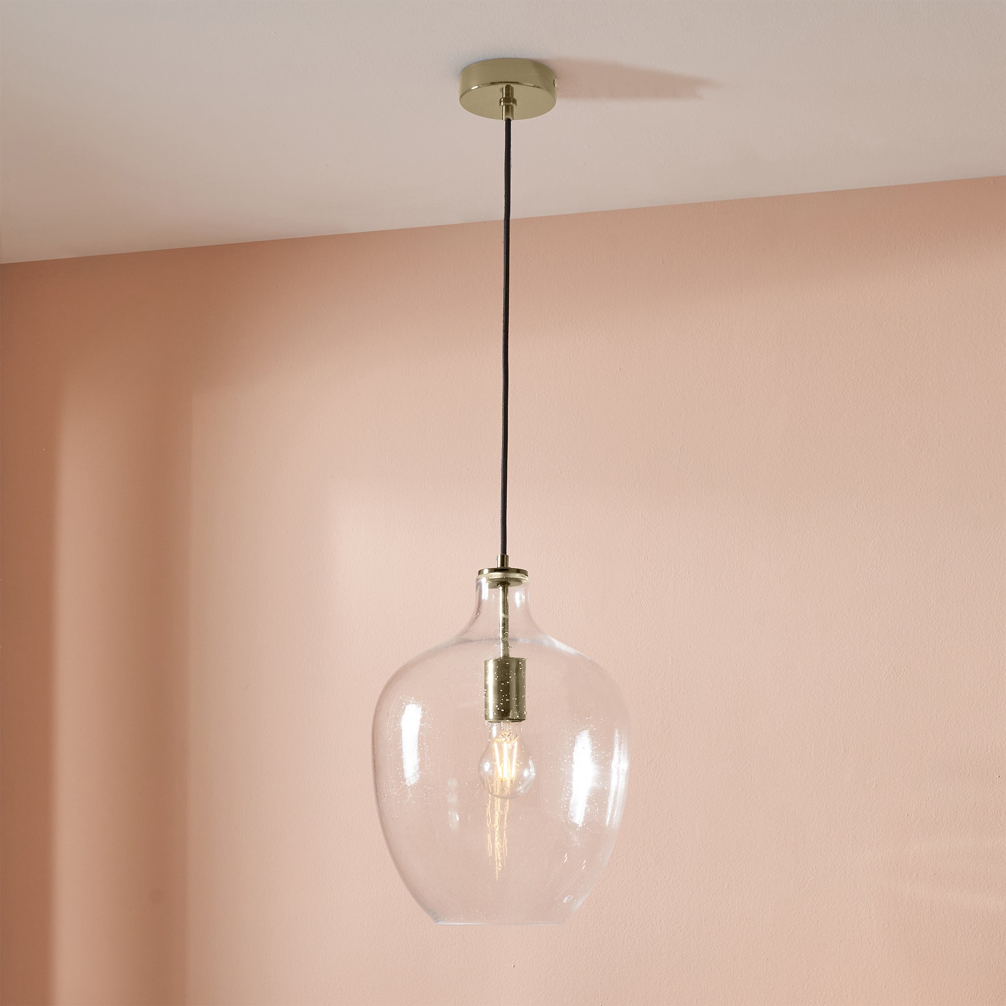 The Pacific Lifestyle Islay Clear Bubble Glass Pendant with a brushed gold bulb holder hangs from the ceiling against a soft pink wall.