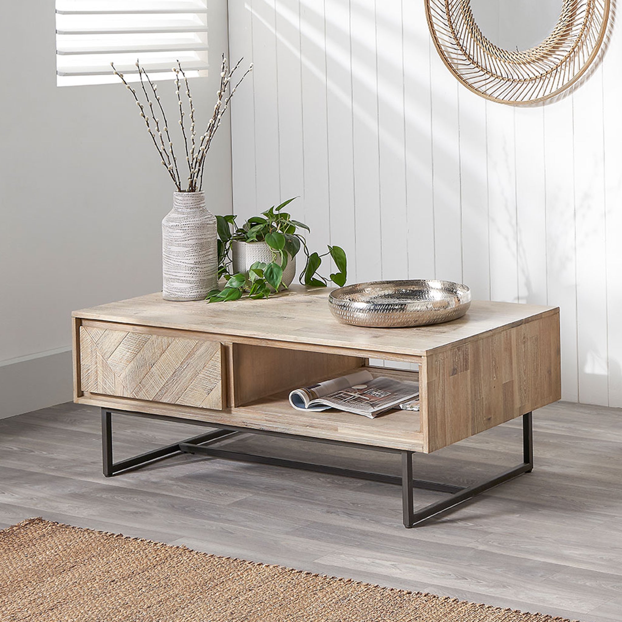 The Pacific Lifestyle - Marca Acacia Wood 2 Drawer Coffee Table features textured wood, metal legs, a decorative bowl, plant, and tall vase in a bright room with white walls. As part of the Acacia Collection, it embodies Scandi styling for modern elegance.