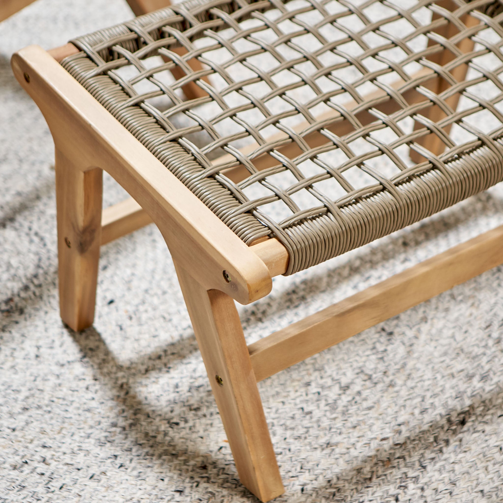 The Pacific Lifestyle Sesto Lounge Chair & Hocker Set boasts an acacia wood chair with a woven rope seat, elegantly complementing a textured gray rug for a perfect addition to your garden furniture ensemble.
