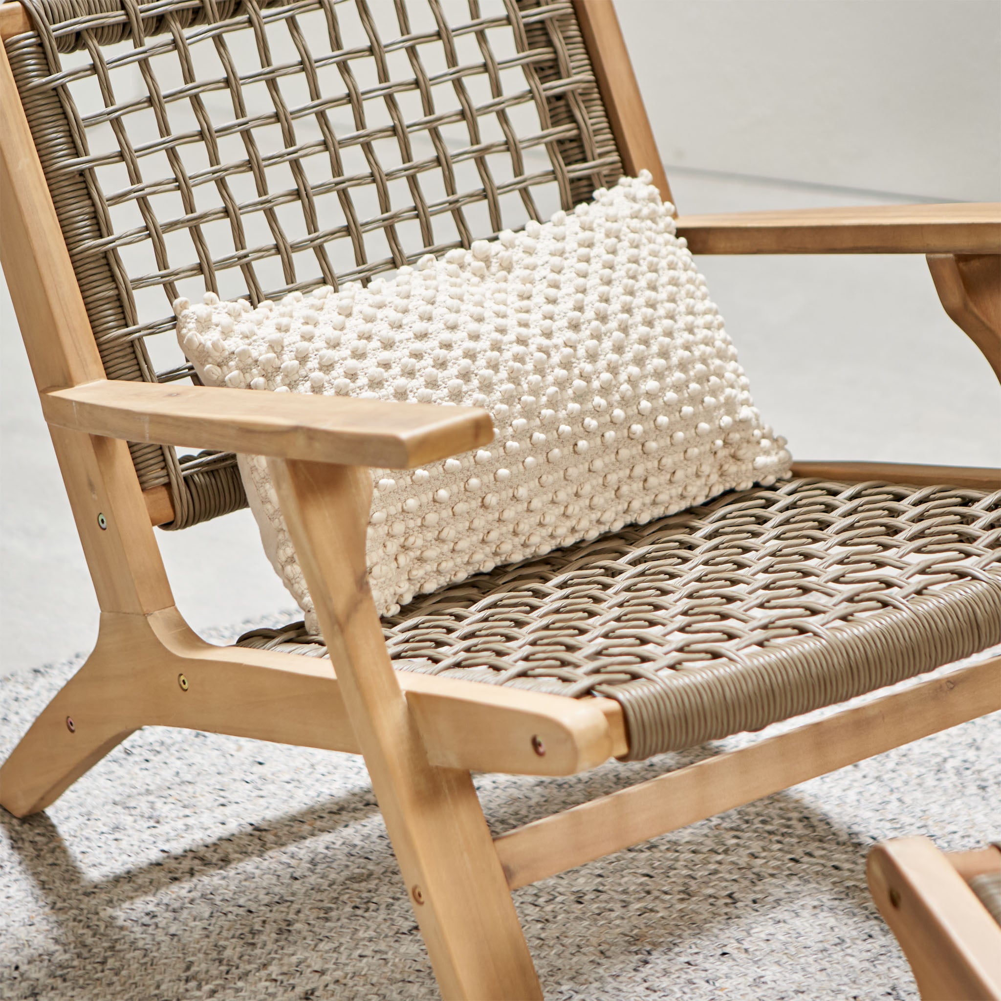 The Pacific Lifestyle - Sesto Lounge Chair & Hocker Set features an Acacia frame, a waterproof woven seat, and a textured white cushion, elegantly situated on a carpeted floor.